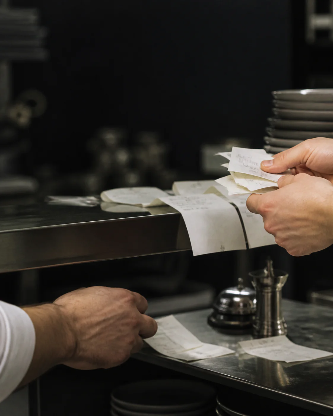 Des mains organisent les tickets de commande sur le passe d'une cuisine